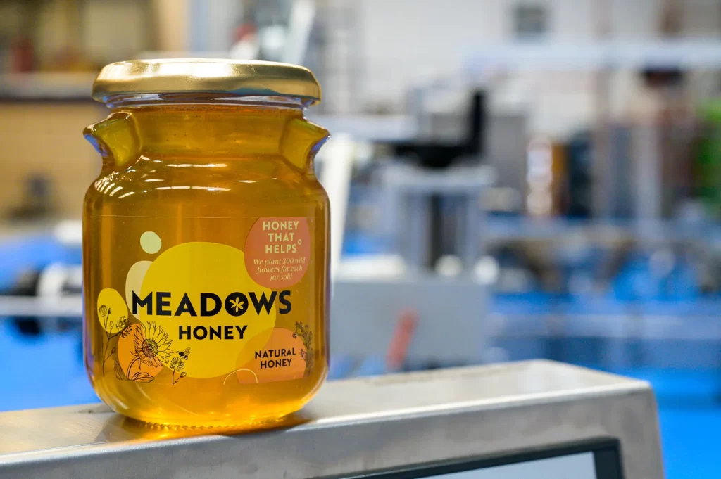 A jar of meadows honey with the factory in the background