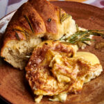 A slice of baked camembert with a warm crust loaf of bread with a balsamic and grape garnish