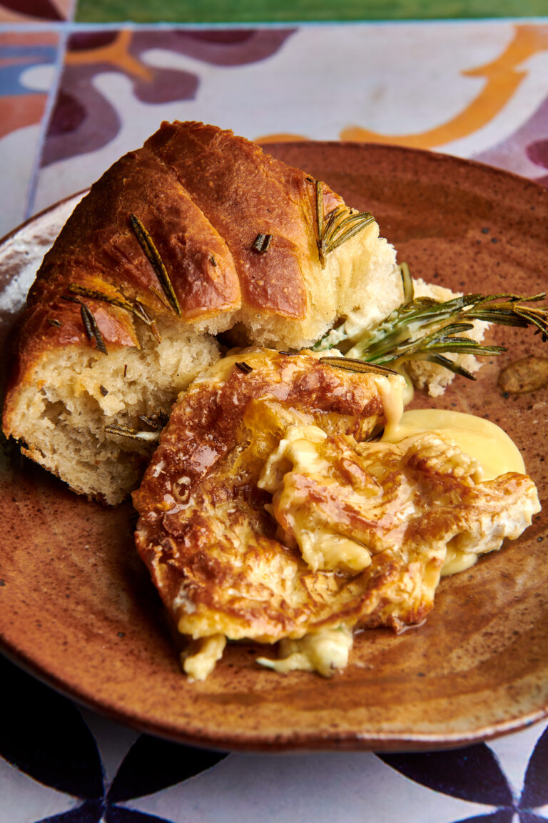 A slice of baked camembert with a warm crust loaf of bread with a balsamic and grape garnish